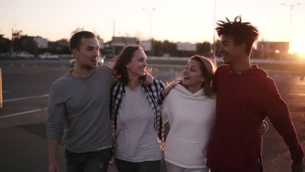 Grupo de amigos de raza mixta caminando abrazándose y hablando juntos en la ciudad. Son dos niñas y dos niños de veintitantos años, conceptos de amistad y estilo de vida, ropa de otoño. Sol brillando fuertemente — Vídeos de Stock