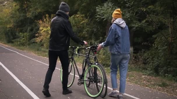 Пара сідає на свої велосипеди. Ранні ранкові велосипеди - двоє людей в осінньому міському парку. Чоловік і жінка їдуть на велосипедах. Активні друзі відпочивають. Повільний рух. Рідкісний вид — стокове відео