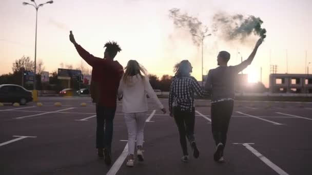 Rare view of two crazy young couples running with colorful smoke bombs in hands on the empty parking zone outside. Emotions, happy lifestyle — Stock Video