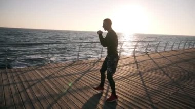 Erkek boxer avcı eğitim açık havada egzersiz görünmez rakip ile yumruk atıyor. Sağlıklı yaşam ve enerji motivasyon - vücut geliştirme kavramı ile denize yakın. Sabah güneş parlıyor