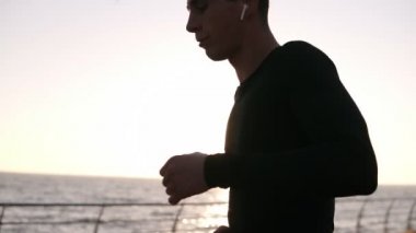 Uzun mesafe çalıştırmadan önce biraz dinlenmek genç jogger durdu. O beyaz kulaklık ile bir spor siyah gömlek giyer. Açık deniz sabahın erken saatlerinde. Güçlü arka plan üzerinde parlayan güneş