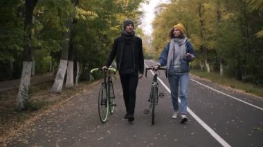 İki yakın arkadaş yeşil ve sarı uzun ağaçlar arasında aktif yaşam tarzı, iletişim, dating, Sonbahar zaman kavramı ile bisiklet Şehir Parkı içinde yürürken çok güzel konuşmayı. Önden görünüm