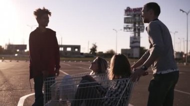 Genç arkadaşlar üzerinde alışveriş sepetlerini eğleniyor. Alışveriş sepeti ile oynayan çok ırklı genç insanlar. Onların kız alışveriş corts yakınındaki Malefriends dururken. Açık havada