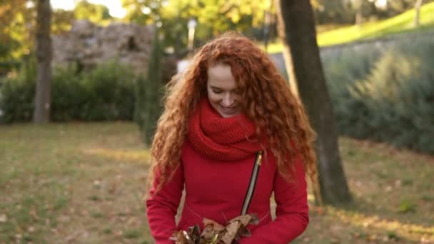 周りの葉を投げ 秋の日に見上げて幸せな赤い頭女の肖像画 都市公園における幸せな若い女に落ちる紅葉し 楽しみに舞っては彼女 笑みを浮かべてください — ストック動画