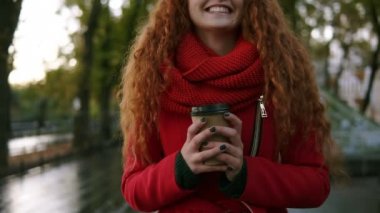 Güzel, heyecanlı genç kadın kırmızı paltolu bir paket servisi olan restoran içki sokak ile yağmurlu bir sonbaharda yürüme. Güzel genç kız gülümseyerek, onun zaman açık havada tadını uzun kıvırcık saçlı. Önden görünüm