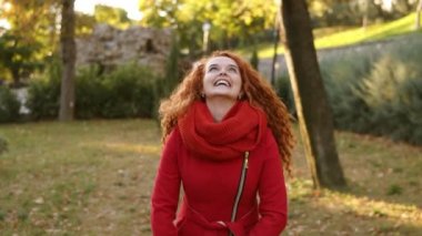 Yaprakları etrafında atma ve sonbaharlar gününde bakarken mutlu bir Kırmızı baş kadın portresi. Şehir Parkı mutlu genç kadın üzerinde düşen sonbahar yaprakları ve onun çevresinde zevk içinde döne döne. Gülümseyen