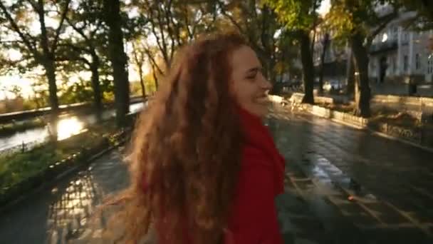 Вид ззаду на молоду кавказьку жінку радісно бігає в барвистому осінньому парку на алеї, насолоджуючись осіннім листям, обертається навколо радісно посміхаючись на камеру. У русі повільний рух — стокове відео