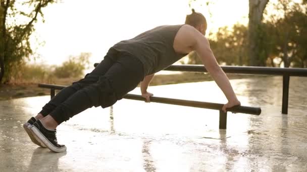 Deporte, fitness, joven musculoso ejercitándose durante un entrenamiento en la calle.Atleta caucásico haciendo flexiones en la barra paralela. El sol de la mañana en el fondo. Vista rara — Vídeos de Stock