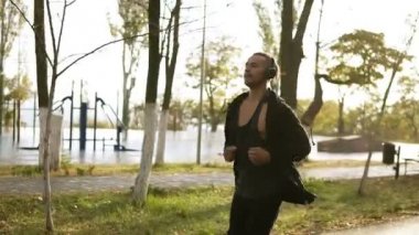 Çalışan ve kulaklıklar ile en sevdiğiniz müzik dinlerken huzurlu adam. Siyah rahat kıyafetler sabah yeşil parkta koşu. Ağır çekim