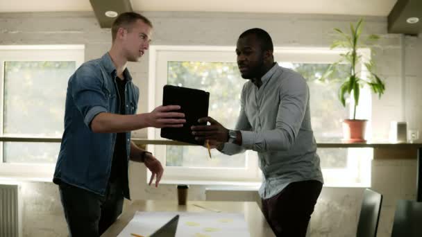 Dois homens estão a pensar e a discutir o projecto. Conceito de trabalho. Plano de marketing pesquisando. Papelada na mesa, tablet preto. Corrida mista. Local de trabalho interior — Vídeo de Stock