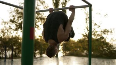 Genç adam açık havada üzerinde yatay çubuk açık havada egzersizleri yapıyor. Jimnastik iş günü paralel enine silah yatay konumda asılı