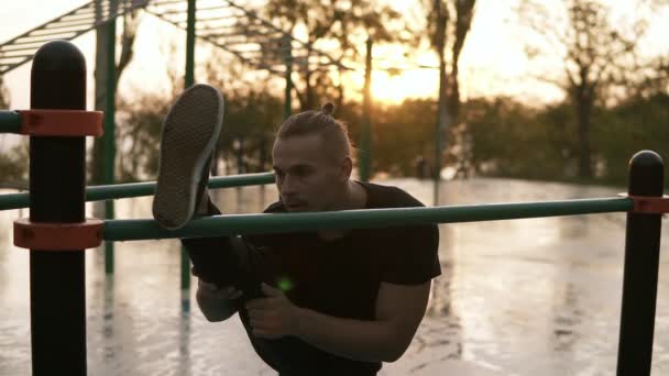 Súlyos izmos sportos kaukázusi Férfi támaszkodva crossbar szabadban lábak nyújtás. Jóképű sportoló bemelegítés, edzés előtt. Sport és fitness koncepció. Reggeli napfelkeltét — Stock videók