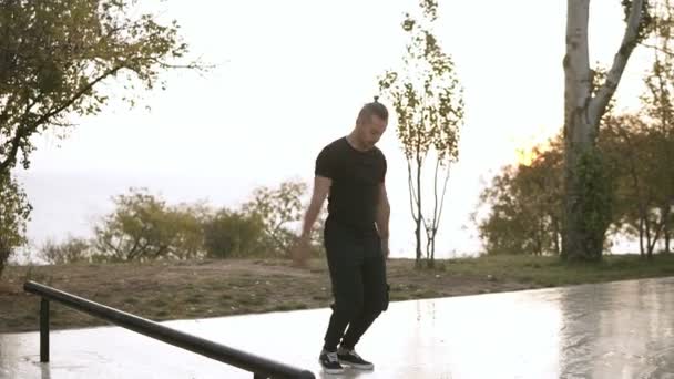 Joven en ropa deportiva negra haciendo ejercicios de estiramiento, calentando las manos. Hombre activo saltando con las manos extendidas antes del entrenamiento principal mientras está parado al aire libre en el parque. Movimiento lento — Vídeos de Stock