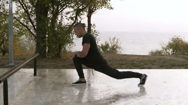 Подтянутый мужчина делает упражнения на растяжку на открытом воздухе, молодой мужчина растягивается и готовится к бегу, привлекательный взрослый бегун растягивает ноги в парке, концепция спортивного фитнеса — стоковое видео