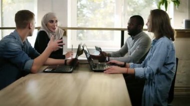 Dört genç grup karışık ırk ve kültür insanlar - Müslüman kadın, Afrika insan ve iki beyaz bir toplantım var birlikte, açık dizüstü bilgisayarlar ile masada oturan ve tartışma, söz var