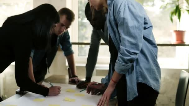 Grupo blanco y negro de personas discutiendo un proyecto en la oficina juntos.Planeando pasos con pegatinas amarillas apuntando a la mesa, escribiendo notas. Un lugar de trabajo brillante. Acelerando el metraje — Vídeos de Stock