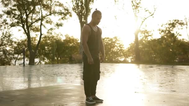 Atletický muž v černém ležérní oblečení provádění akrobacie vyletí a kotrmelec venkovní - zpomalený stedycam. Ranní slunce svítí na pozadí — Stock video