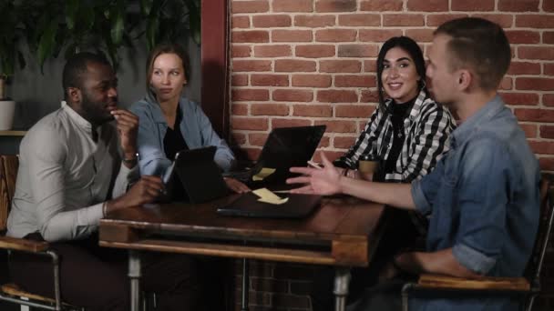 Jovens misto correu pessoas usando laptops. tablets e smartphones sentados no local de trabalho, jovens multi-étnicos trabalhando em equipe com dispositivos em reunião em local público dentro de casa, discutindo o trabalho — Vídeo de Stock