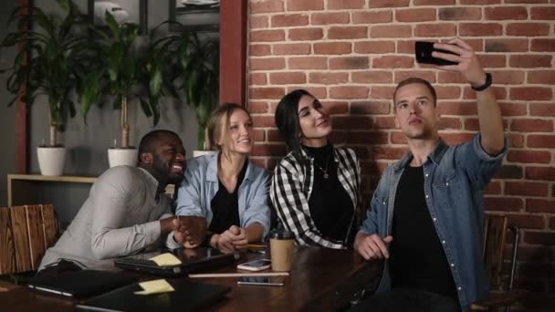 Kavkazská muž vezme skupina selfie na schůzce s rozmanitou přáteli v coffeeshop nebo na pracovišti, mnohonárodnostní mladí lidé dělat fotografie spolu v kavárně s cihlovou zeď interiéru, multietnické šťastný — Stock video