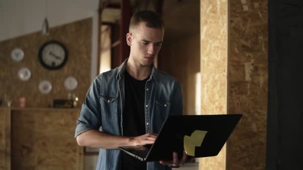 Attraktiva koncentrerad ung affärsman är promenader med en laptop i handen och att skriva. Kaukasiska man som arbetar i offentlig arbetsplats med tegel vägg interiör — Stockvideo