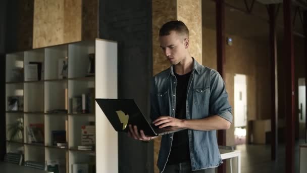 Attraktiva koncentrerad ung affärsman är promenader med en laptop i handen och att skriva. Kaukasiska positiva man som arbetar i offentlig arbetsplats med tegel vägg interiör. Slow motion. Framifrån — Stockvideo