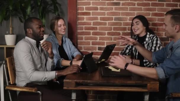 Young positive group of four mixed raced people using laptops. tablets and smartphones sitting at workplace, multi-ethnic young people at meeting in public place indoors, discussing work issues — Stock Video