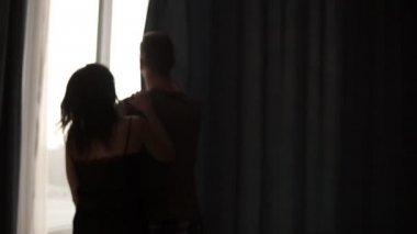 Sabah yürüyüş yatağı ve açık genç güzel çift pencere, sarılma ve kadın bakan perdeler, koca elleri atlamak. Mutlu sabah birlikte. yakın çekim