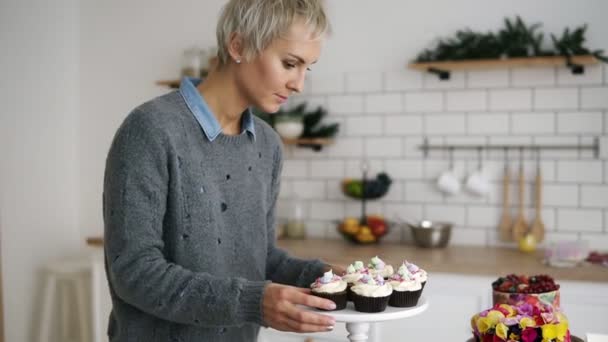 Konditorin in ihrer Küche mit selbst gebackenen Muffins und Kuchen. Fantasievoll dekoriertes Gebäck auf dem Tisch. Zeitlupe — Stockvideo