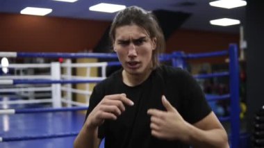Modern bir spor salonu boks ringde yakınındaki eğitim agresif uzun saçlı adam. Gölge mücadele. Siyah tişört ve siyah saçlı eğitim kick boks. Terli, kızgın yüzü yakın çekim