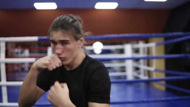 Kavkazské mladík školení na boxerský ring v moderní tělocvičně. Boj stínem. Kickboxer v černé tričko a dlouhé vlasy školení. Detailní záběr — Stock video