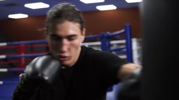 Determinated kickboxer träffar boxning päron. En arg boxare sätter en punch i en boxning väska i svarta handskar. Träningspass i gymmet. Slow motion — Stockvideo
