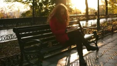 Genç bayan bir kitap okuma, kırmızı kafa güzel kız oturan park bankında, sonbahar renkli sahne, Mercek Parlaması, Şehir Parkı sakin ol. Özet görüntüleri.