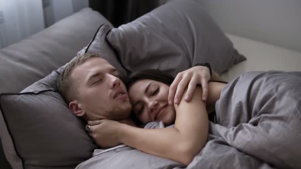 美丽的夫妇微笑着拥抱, 而在一起的时间在家里的床上。男人醒来后正在亲吻他的女朋友或妻子 — 图库视频影像