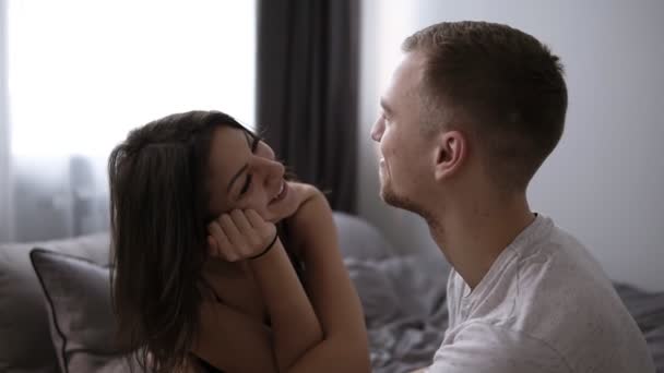 Lyckliga älskande par avkopplande på säng hemma, ung man röra leende vacker kvinna ben, tittar i ögonen strök smekande, njuter av samhörighet — Stockvideo