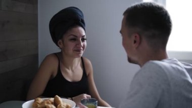 Banyo havlusu başında çekici genç kadın ile onun erkek arkadaşı ya da kocası mutfak masasında oturuyor. Kahvaltı. Kız kocasına yüzüne yakın bir şey söylemeye çalışıyor