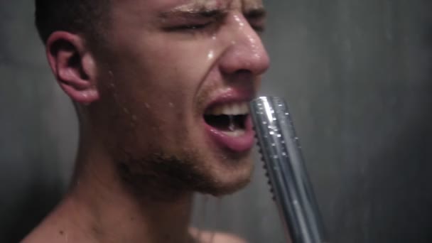 Imágenes de cerca de un hombre cantando emocionalmente y en voz alta en la ducha usando el cabezal de la ducha con agua corriente en lugar de un micrófono — Vídeo de stock