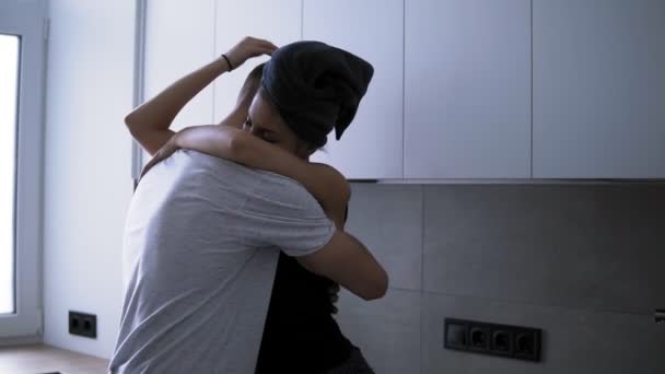 Pareja romántica joven en la cocina. Sexy joven mujer está en ropa doméstica y toalla de baño en la cabeza con su hombre guapo están pasando tiempo juntos, abrazos. Mujer sentada encima — Vídeos de Stock