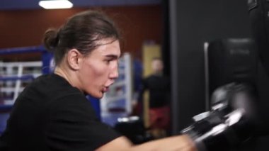 Armut boks siyah T-shirt sayısı tespit, agresif boksör görüntülerini kapatın. Kızgın bir boksör siyah eldiven bir yumruk boks çantaya koyar. Spor olarak çalışma. Terli yüz. Ağır çekim. Yan