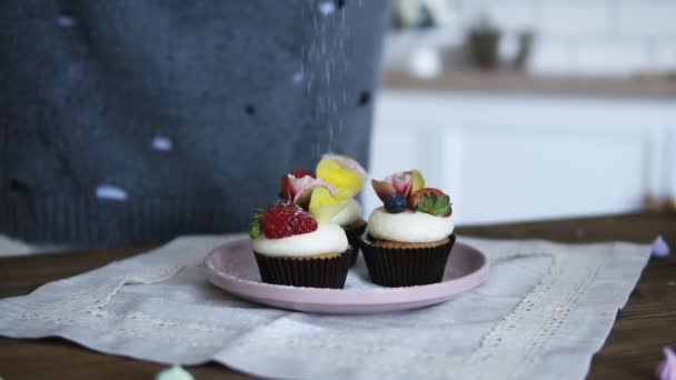 Ζαχαροπλάστης διακόσμηση νόστιμα, φανταχτερά διακοσμημένα cupcakes. Ζάχαρη άχνη σκορπιστεί στο κέικ με φρέσκιες φράουλες και κρέμα στην κορυφή. Μπροστινή όψη. Αργή κίνηση — Αρχείο Βίντεο