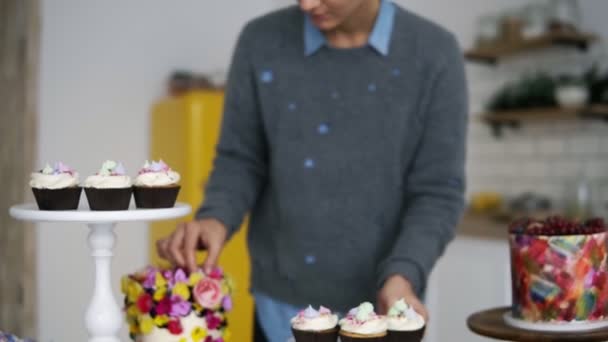 Young grey haired woman decorating cupcakes with colored marshmallows. Beautiful confectioner at her modern kitchen studio — Stock Video