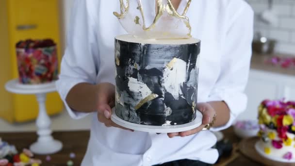 Θηλυκό ζαχαροπλάστη παρουσιάζοντας διακόσμηση κέικ στην κουζίνα της, κρατώντας το με τα χέρια απλωμένα. Με στόχο την εστίαση του κέικ. Μπροστινή όψη — Αρχείο Βίντεο