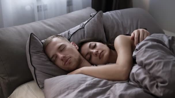 Retrato de jovem casal caucasiano dormindo na cama em casa nos lençóis cinzentos. Hora da manhã — Vídeo de Stock