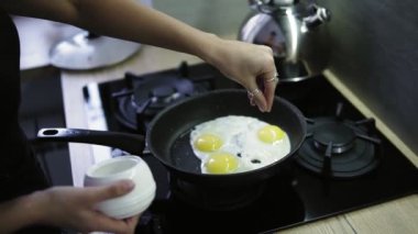 Karanlık banyo havlusu başında genç çekici kadın iki kişilik kahvaltı hazırlıyor. Pan kızarmış yumurta, yumurta kız tuzlama