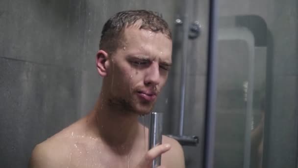 Портрет мужчины, поющего эмоционально в душе, использующего душевую головку с текущей водой вместо микрофона — стоковое видео