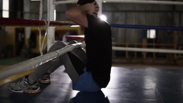 Boxer auf dem Boden am Boxring beim Training der Bauchmuskeln. Oberkörper bis zu den Boxseilen heben. Trainingsprozess im Boxstudio. Seitenansicht — Stockvideo