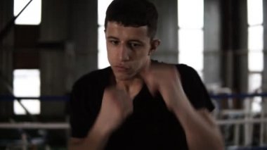 Siyah T shirt genç adam darbeler, ciddi spor salonunda kamera seyir sırasında yumruklar yerine getirir. Egzersiz boksör yorgun yakın çekim