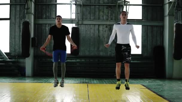 Retrato de dos jóvenes boxeadores caucásicos saltando usando una cuerda de salto mientras se calientan en el estudio de boxeo-gimnasio. Haciendo saltos altos sincrónicamente. Longitud completa, cámara lenta — Vídeos de Stock