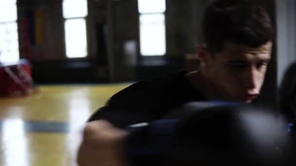 坚定的年轻拳击手打黑色袋在老式风格的健身房 白种人年轻人打在黑色手套的打气筒 — 图库视频影像