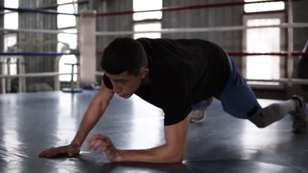 Primer plano del joven deportista musculoso haciendo flexiones, desde los codos hasta las manos extendidas, mientras hace ejercicio en el gimnasio de boxeo — Vídeos de Stock