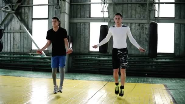 Os jovens boxeadores caucasianos estão pulando usando uma corda de salto enquanto se aquecem no estúdio de boxe ginásio. Comprimento total, vista frontal — Vídeo de Stock